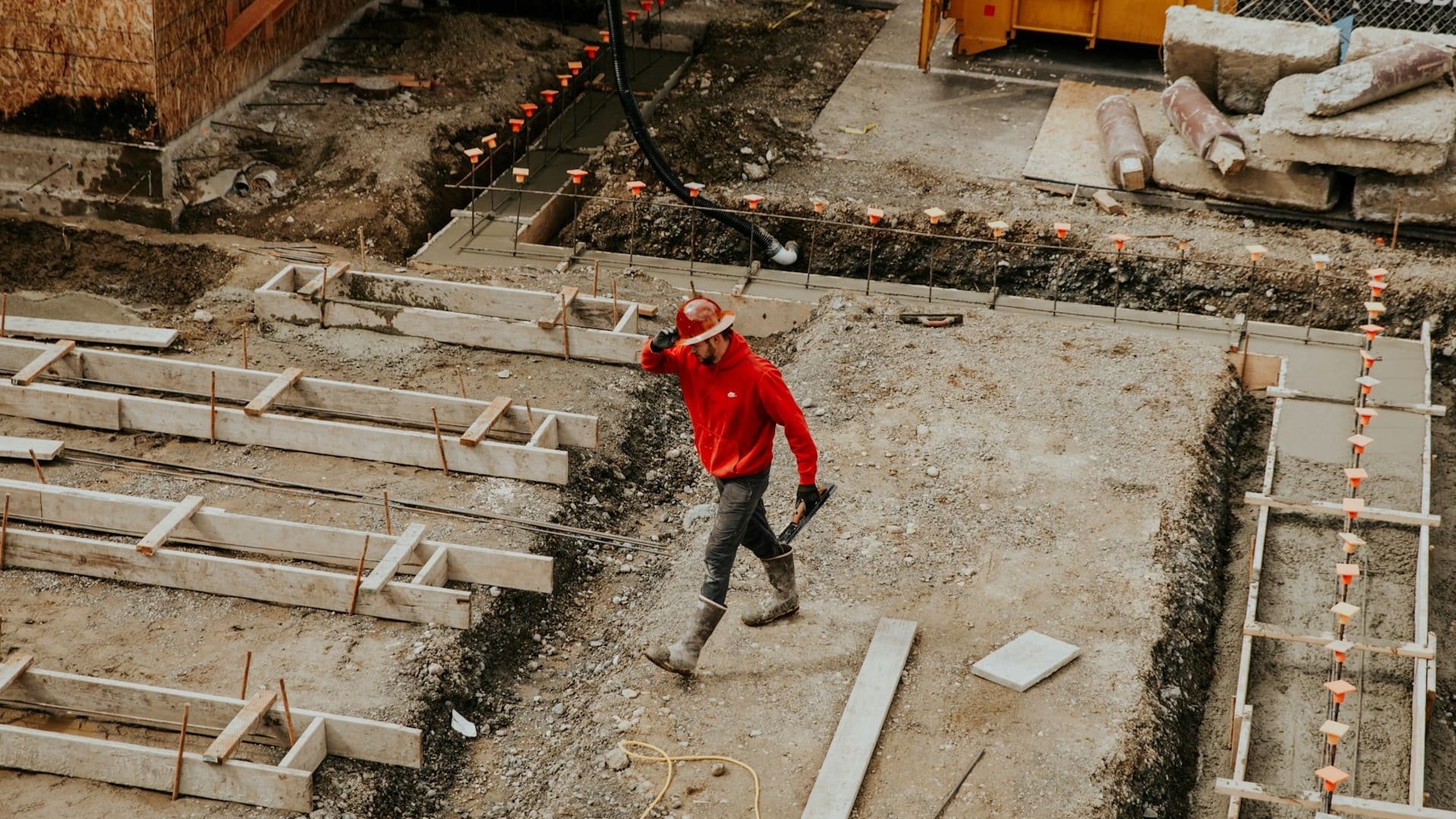 Aannemer op bouwplaats met funderingswerkzaamheden, draagt veiligheidsschoenen en helm &ndash; wettelijke verplichtingen aannemer