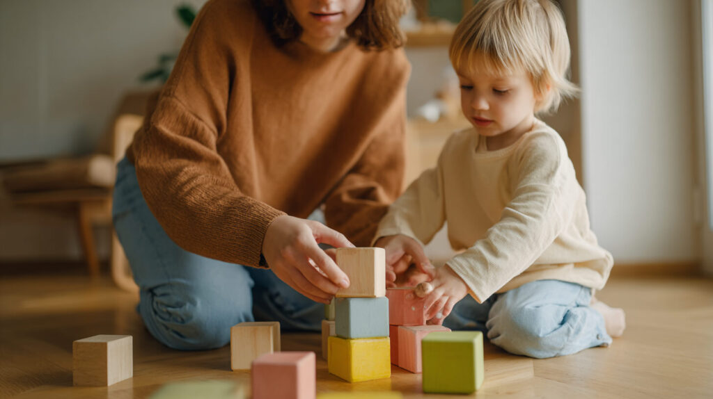 Ouder en peuter stapelen samen gekleurde houten blokken op de vloer van een kinderopvanglocatie