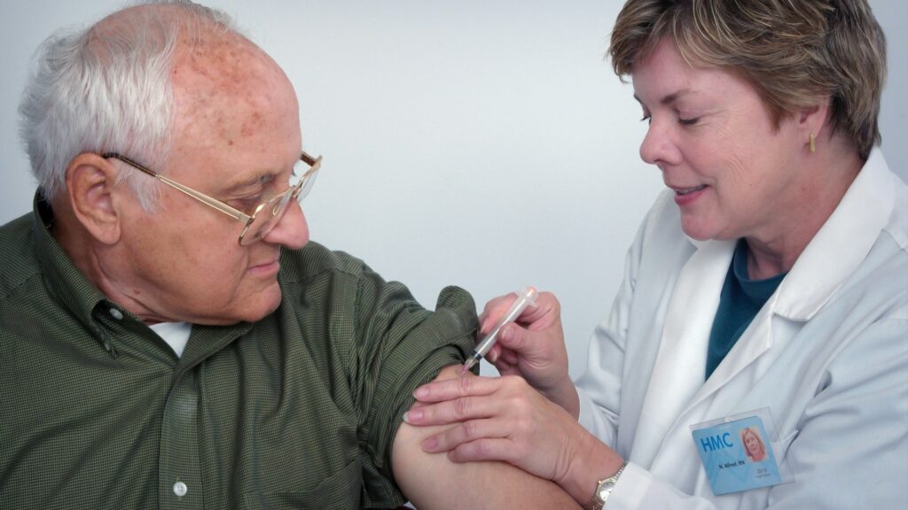 Verpleegkundige geeft injectie aan oudere man tijdens thuiszorg volgens thuiszorg regels Nederland