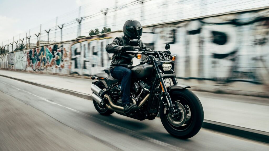 Motorrijder met beschermende motorkleding rijdt langs een muur met graffiti