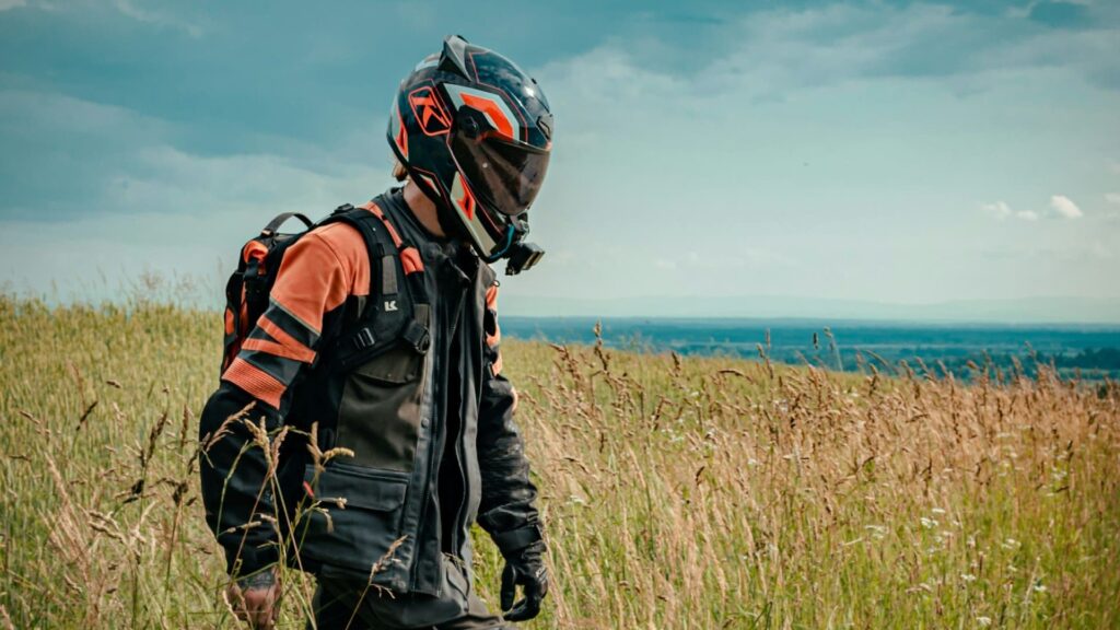 Motorrijder met helm en beschermende motorkleding loopt door hoog gras in open landschap