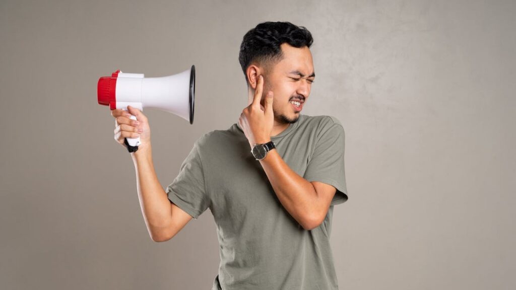Man houdt een megafoon bij zijn oor en kijkt geïrriteerd weg vanwege geluidsoverlast.

